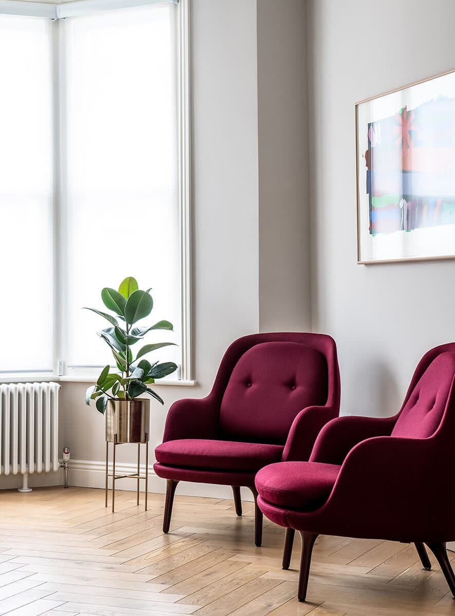 Jasny salon z bordowymi fotelami klubowymi i rośliną przy oknie — realizacja KR-BUD w Puławach